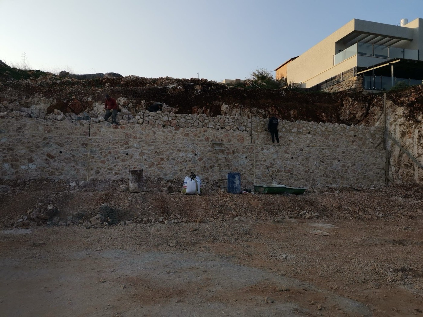 חפירה וקירות תמך: פתיחת המגרש במדרון וקיר אבן לכל אורכו.